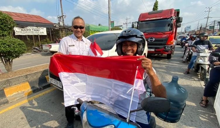 Kepala Diskominfo Staper Kutim Ronny Bonar H Siburian saat memberikan bendera kepada warga yang tengah melintas